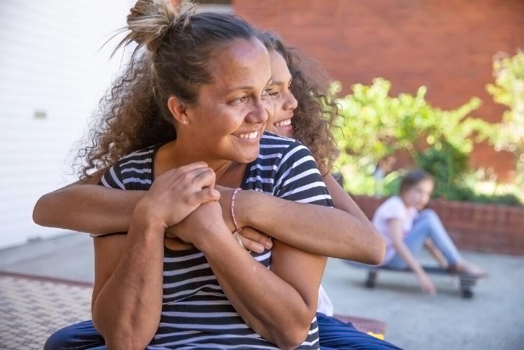 Girl and woman smiling, hugging, looking to side of camera